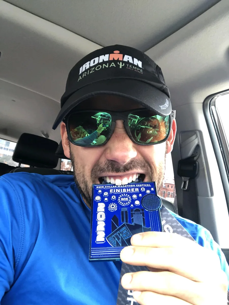 Chris Leach holding a BMW Dallas Marathon Festival 50K finisher medal