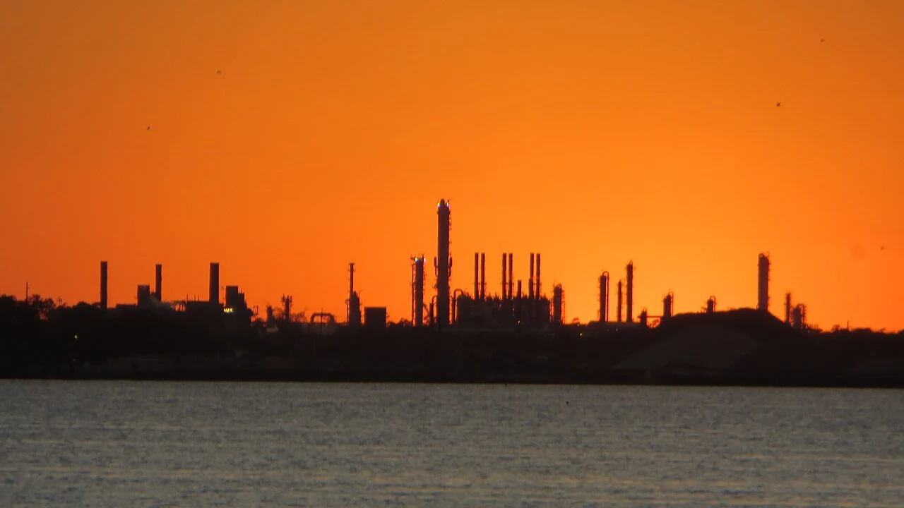 Industrial towers silhouetted against an orange sunset across the water at Lake Charles